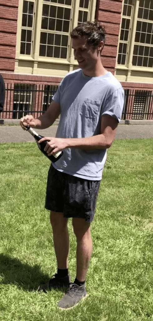 Image of newly graduated PhD student opening a bottle of champagne